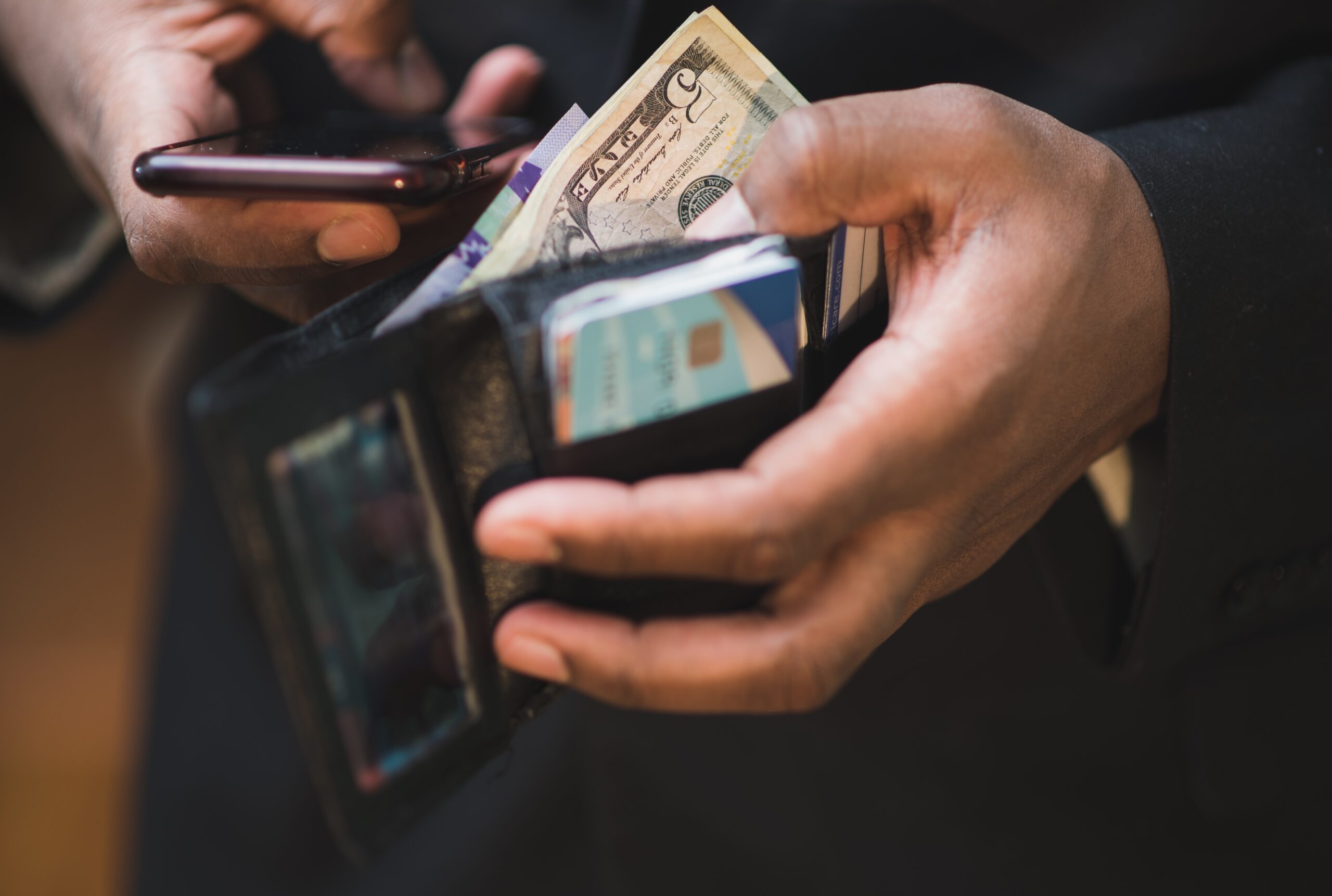 Camera is zoomed in on a Black man holding a phone in one hand and his open wallet in the other, symbolizing financial stress and mental health.